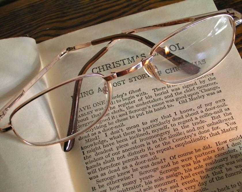 The book A Christmas Carol is open with glasses lying on the pages